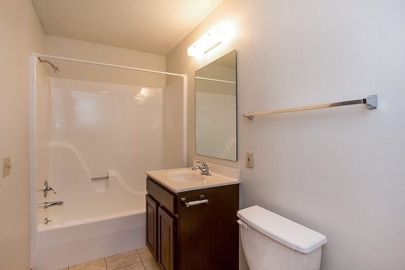 Small bathroom with a shower-tub, vanity, mirror, and toilet, shown in warm lighting.