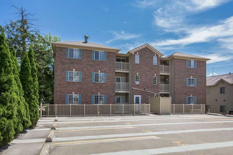 Brick apartment building with balconies and a parking lot in front under a clear sky