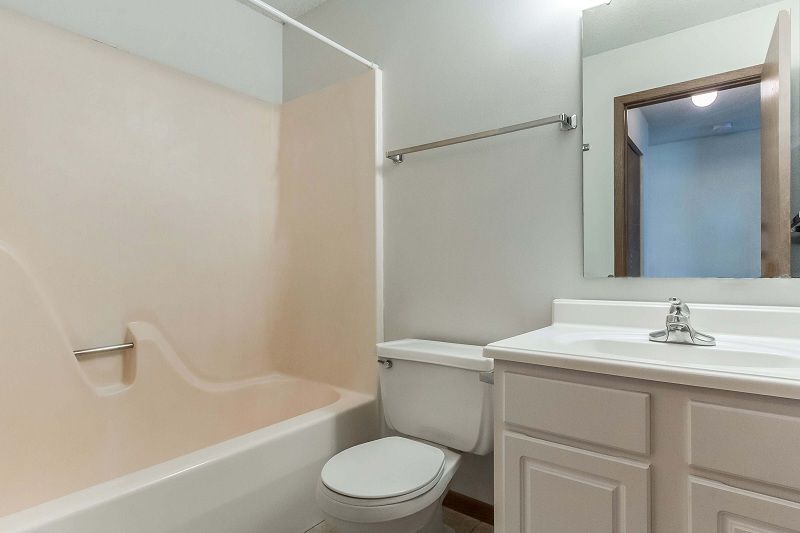Small bathroom with tub, toilet, and sink vanity in white and beige.