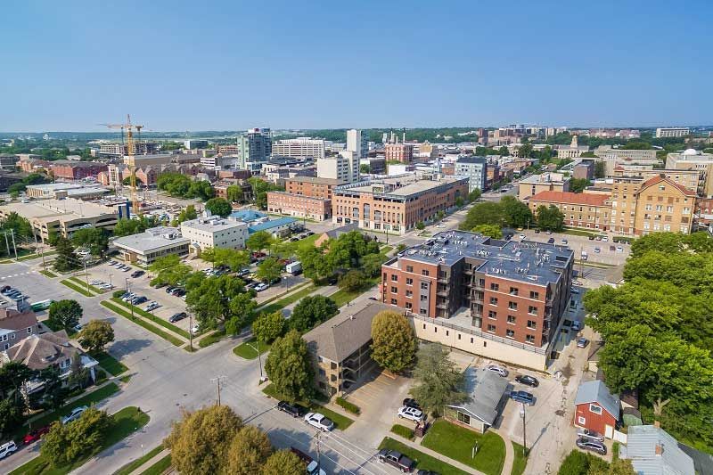 Aerial view of a city center with streets, trees, low-rise buildings, and a clear blue sky.