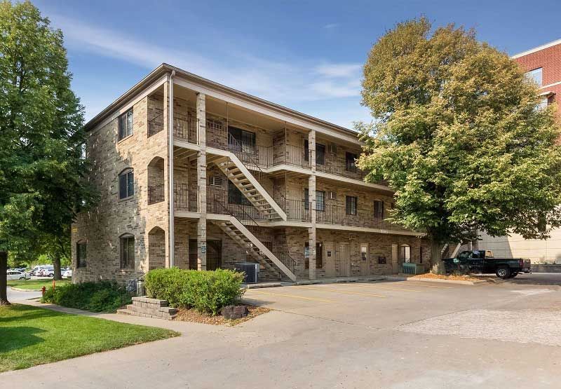 Three-story stone apartment building with outdoor staircases and trees in front