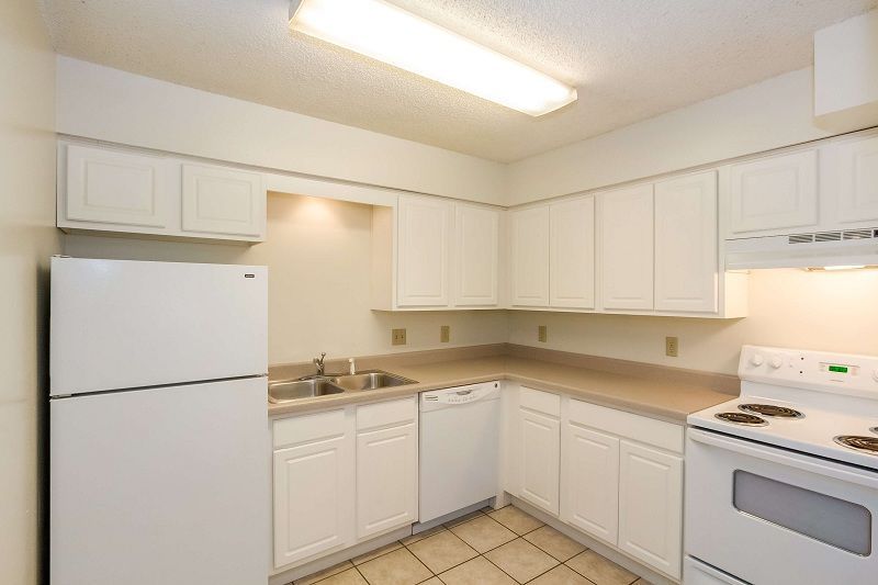 Bright white kitchen with refrigerator, sink, cabinets, stove, and tiled floor