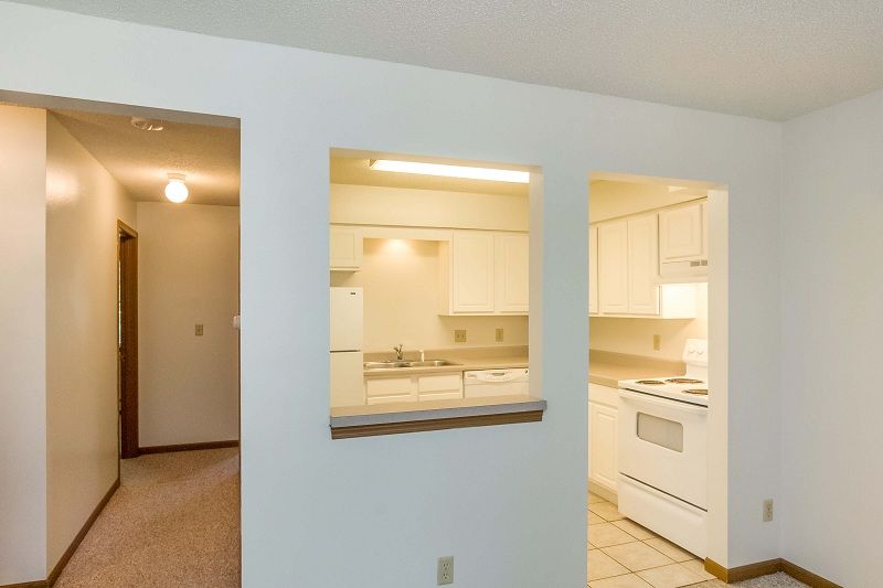 Bright apartment hallway with a pass-through opening to a white kitchen and tiled floor