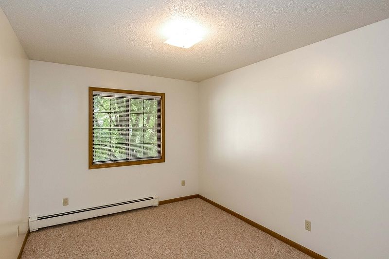 Empty beige bedroom with white walls, window blinds, carpet, and ceiling light