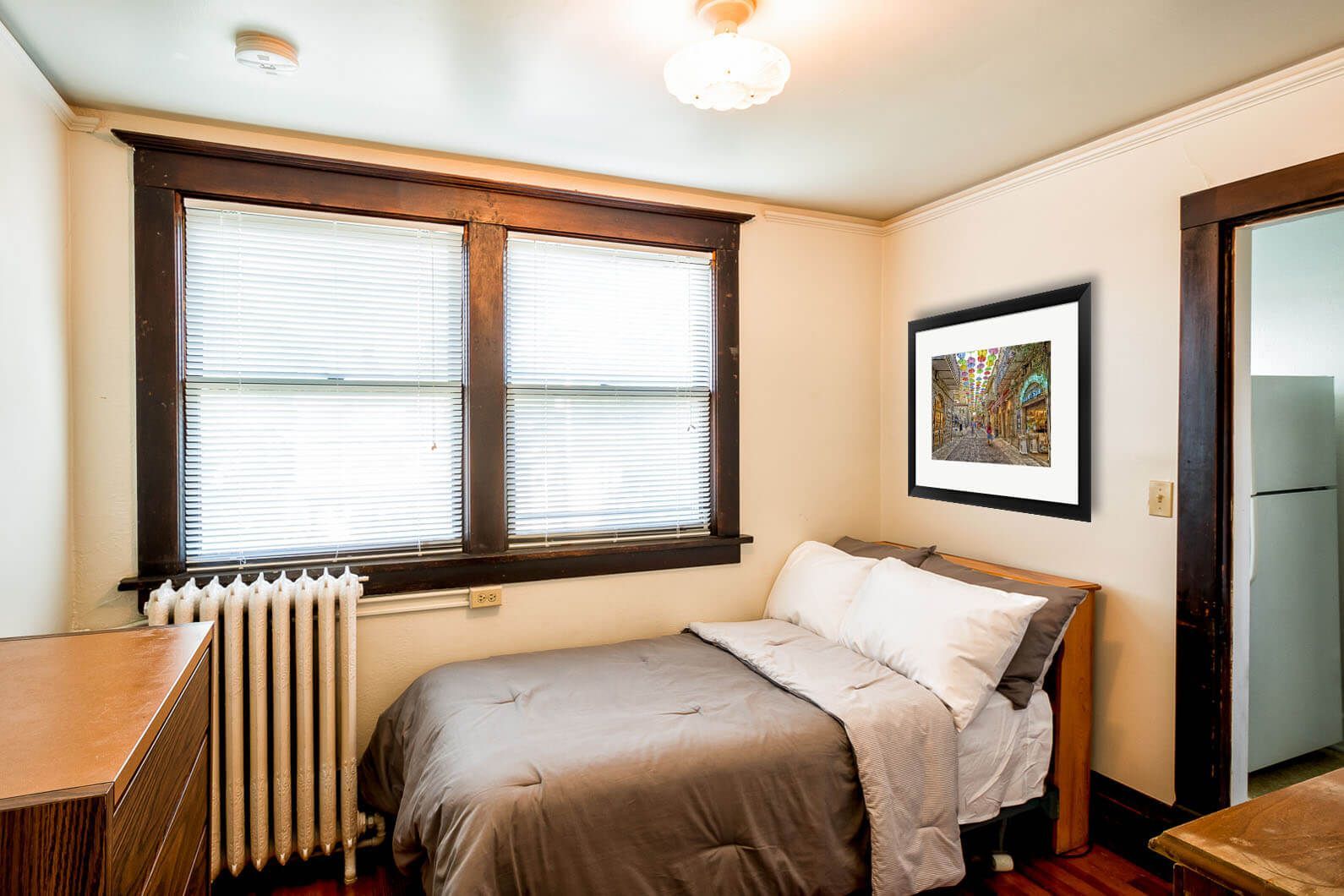 Small bedroom with a bed, two windows, radiator, and framed wall art