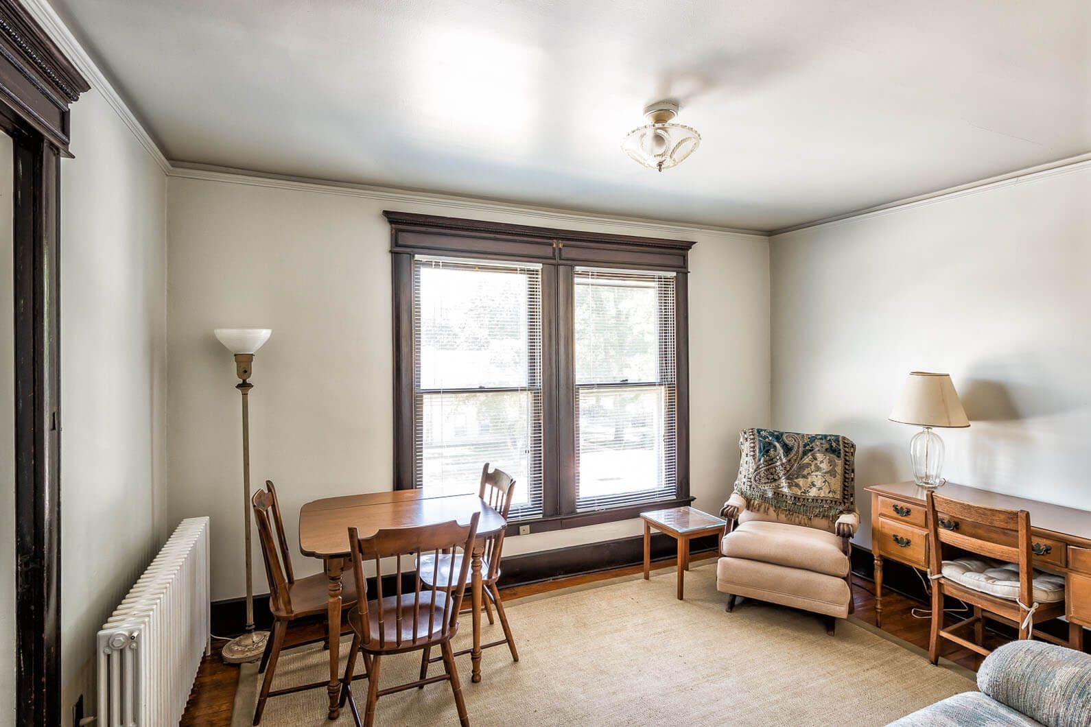 Bright living room with large windows, beige walls, a floor lamp, chairs, and a small table