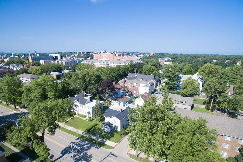 Aerial view of a tree-lined neighborhood with houses, streets, and a distant city skyline