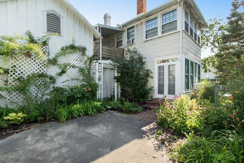 White house exterior with ivy-covered walls, garden greenery, and a paved driveway in front.