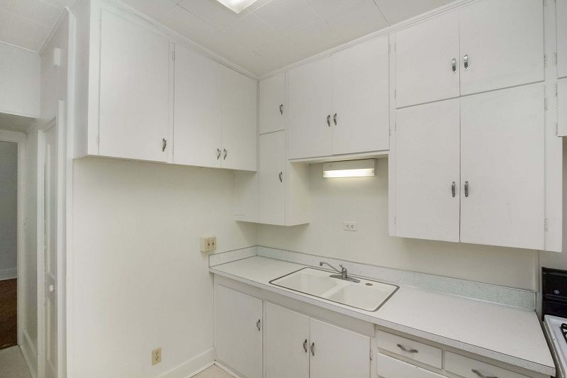 Bright white laundry room with cabinets, countertop, sink, and overhead light.