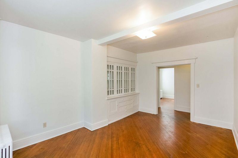 Empty white room with hardwood floors, built-in glass cabinets, and an open doorway to another room