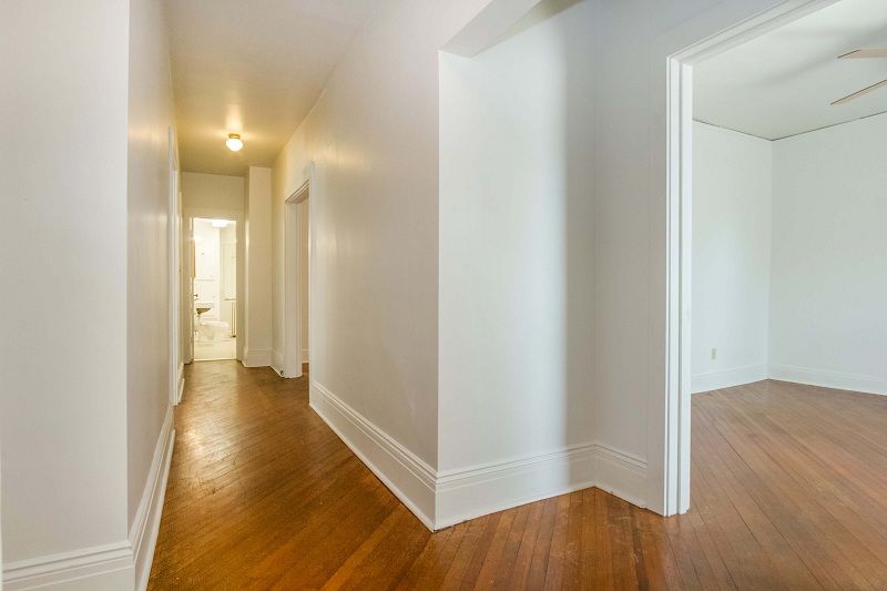 Bright hallway with hardwood floors and white walls, opening into an empty room on the right.
