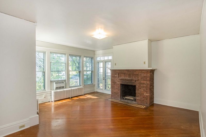 Empty living room with hardwood floors, brick fireplace, and large windows