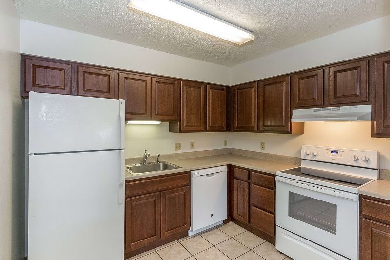 Small kitchen with brown cabinets, white appliances, beige countertop, and tiled floor.