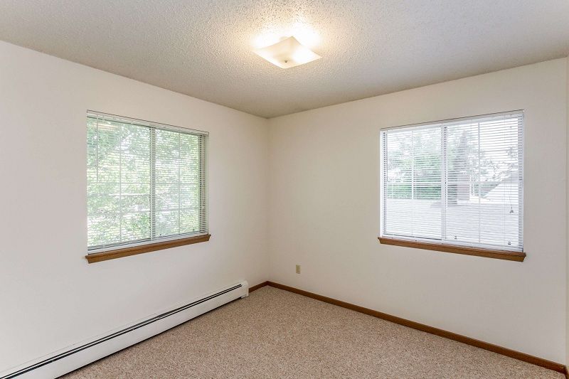 Empty beige room with two windows, white blinds, and a ceiling light.