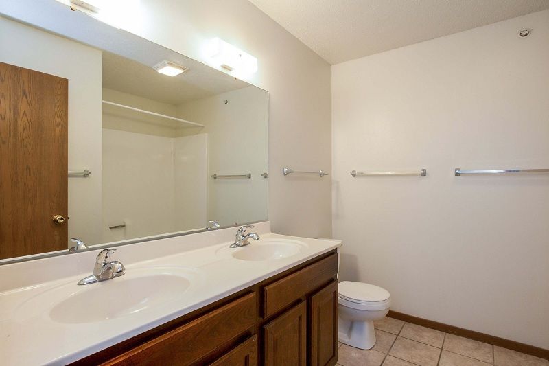 Bathroom with large mirror, double sink vanity, toilet, and beige tile floor.