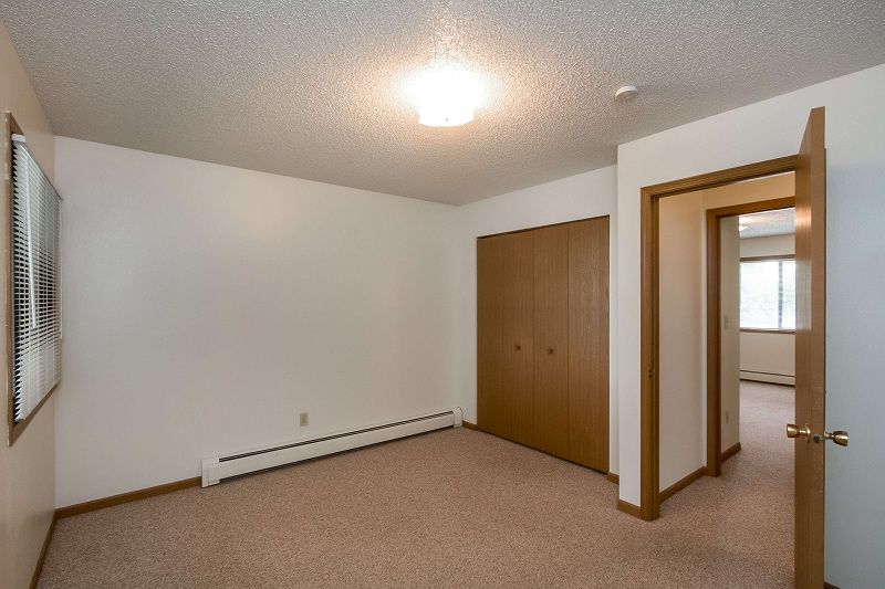 Empty beige bedroom with closet, open doorway, and window blinds