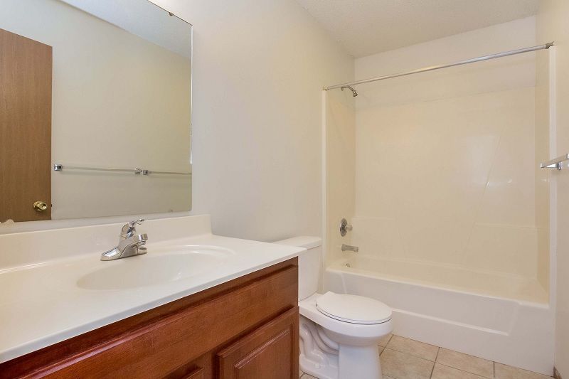 Bathroom with white tub, toilet, sink, wood vanity, and wall mirror.