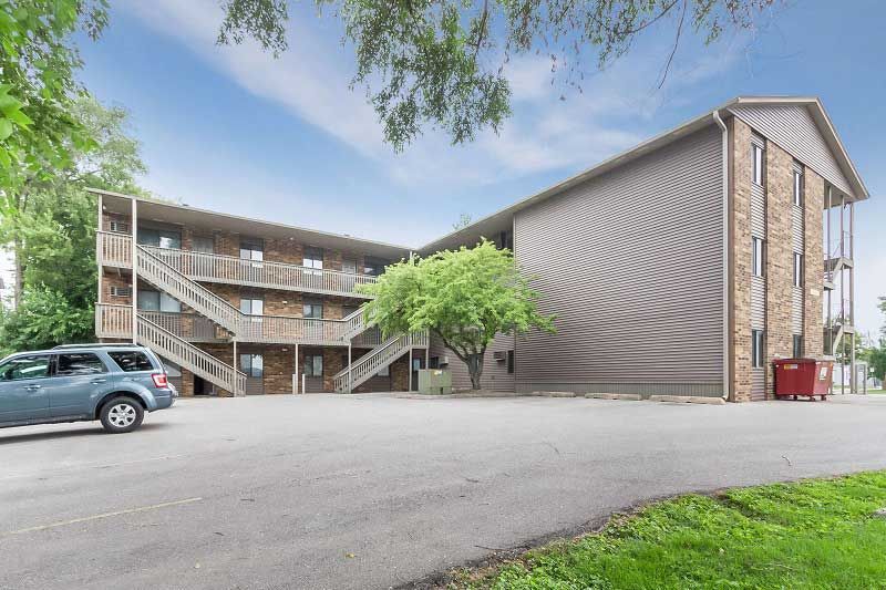 Apartment building exterior with parked cars, outdoor stairways, and a grassy foreground