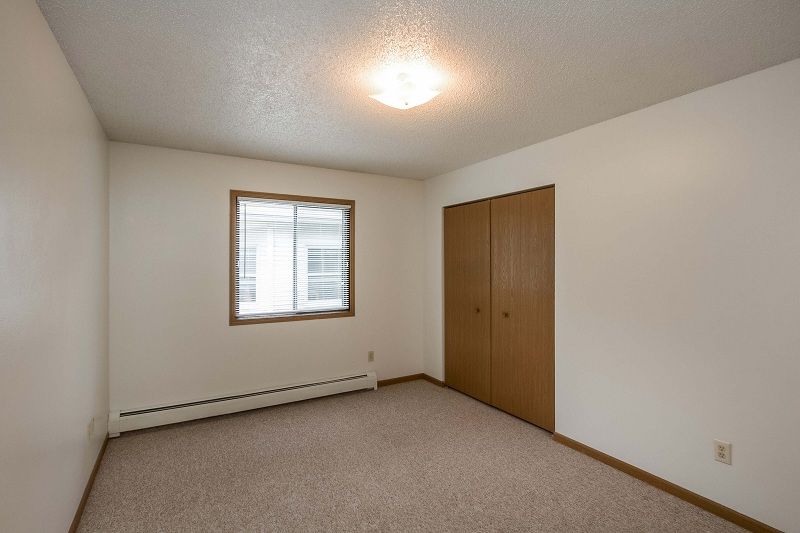Empty beige bedroom with window, closet doors, and carpeted floor