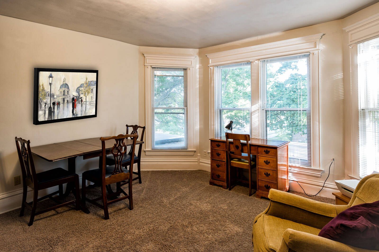 Bright living room with large windows, dining table, wooden desk, and yellow armchair