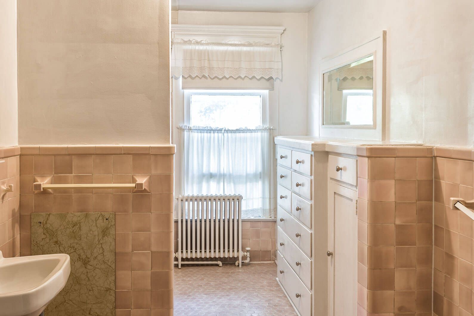 Bright bathroom with pink tile, white vanity, window, radiator, and mirror.