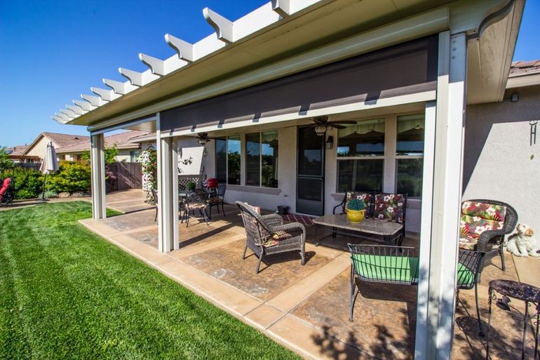 Patio with pergola, brown retractable shade, and outdoor furniture on a sunny day.
