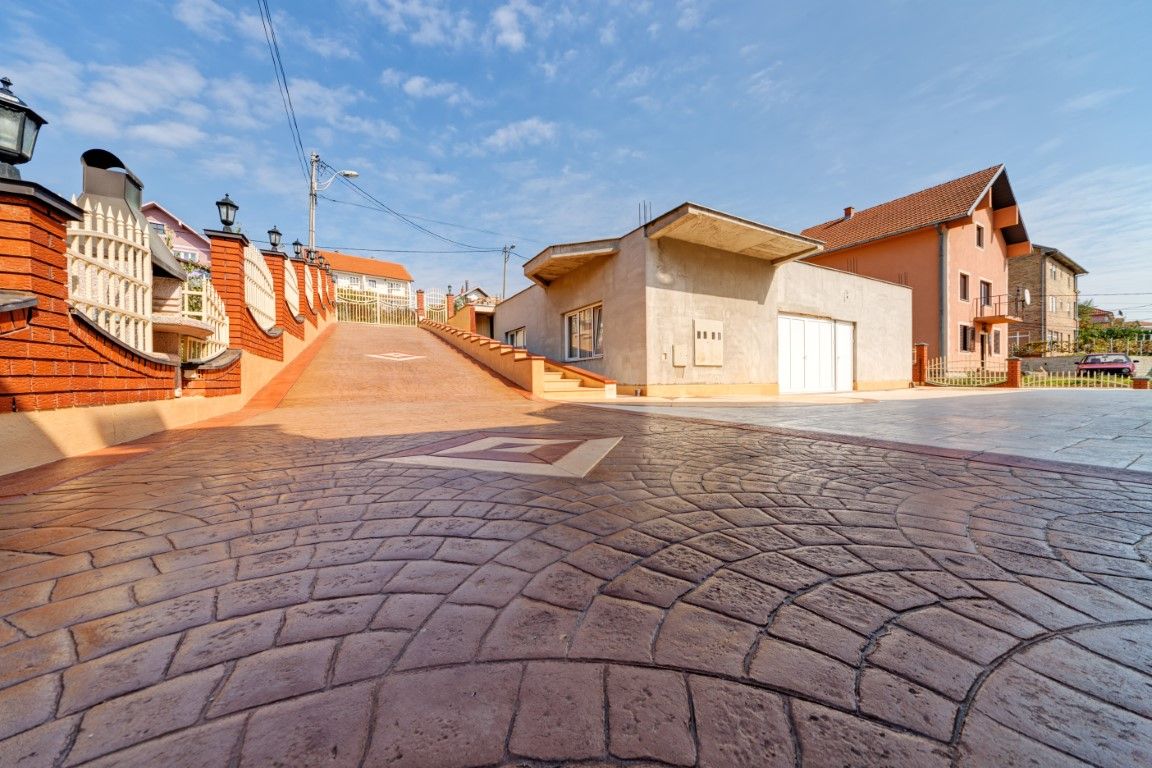 Brick-paved driveway leading uphill past buildings with red roofs and a clear blue sky.