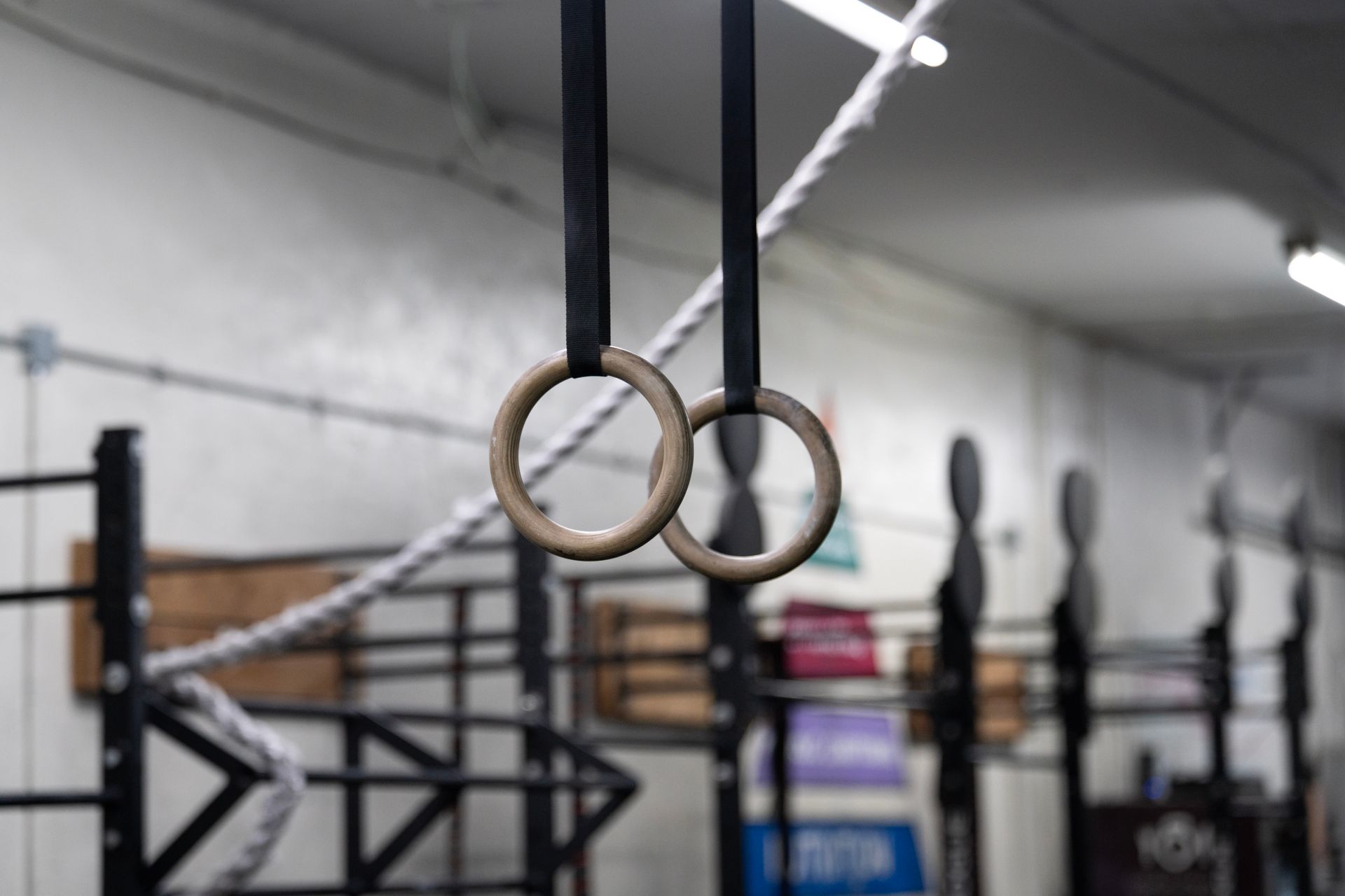 Gymnastic rings hanging in a gym with equipment blurred in the background