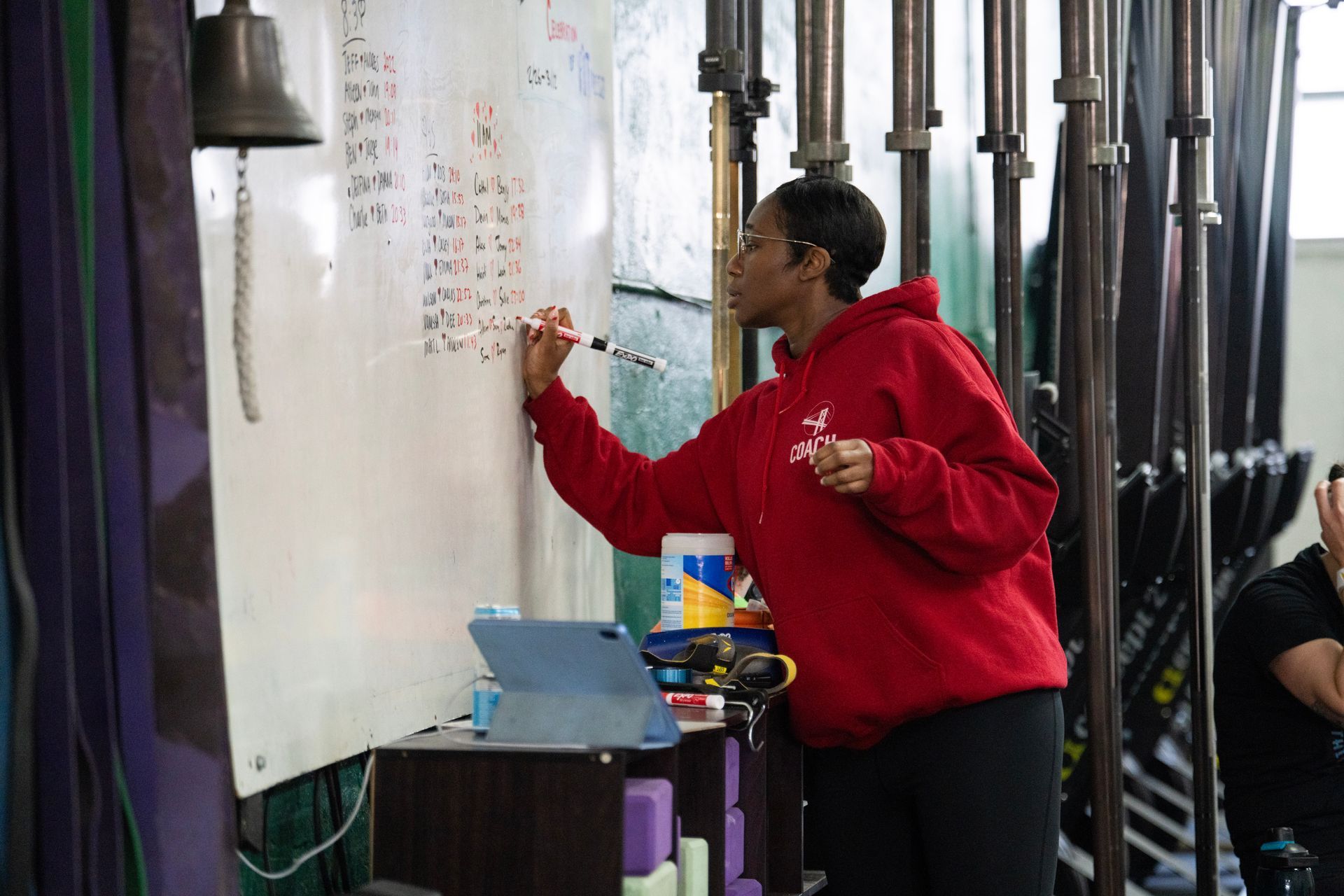 Person in red hoodie writing on a whiteboard in a gym-like space