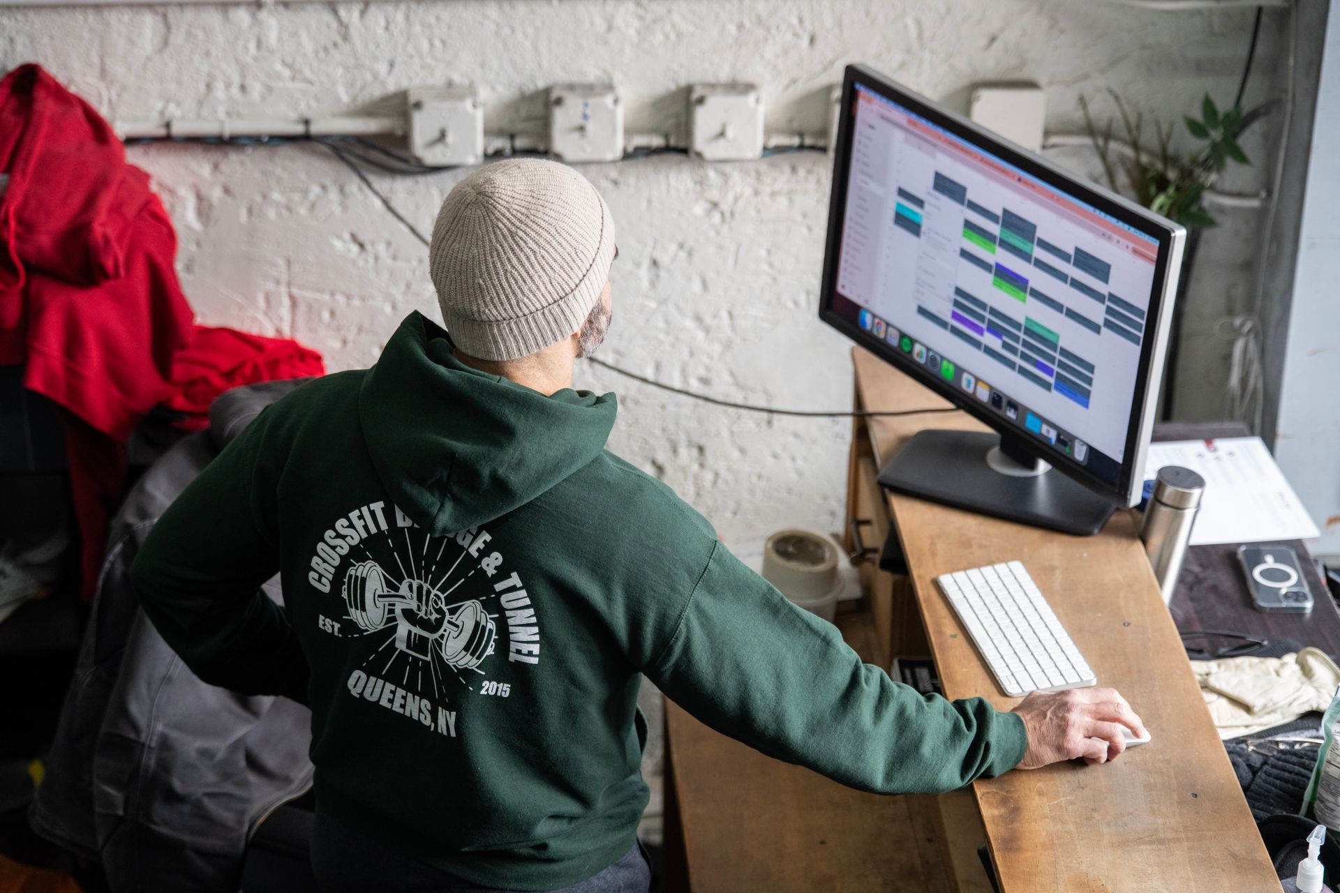 Person in green hoodie working at a desktop computer in a small, rustic room