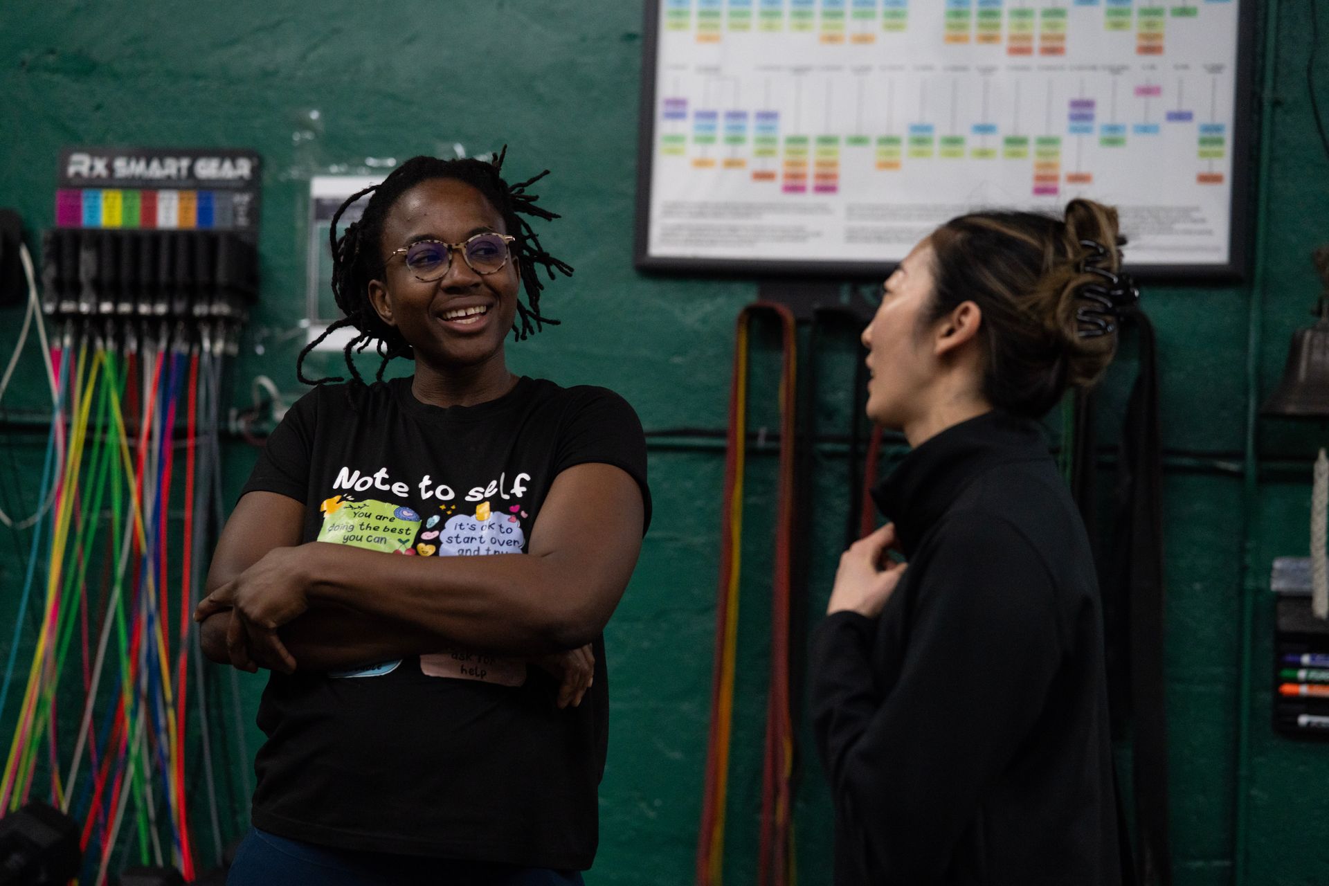 Two people talking in a classroom, standing by colorful wall charts and markers.