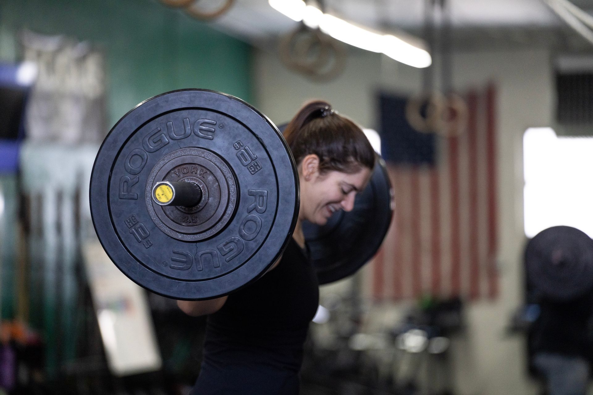 Man lifting a barbell in a gym, bent forward with focused expression.