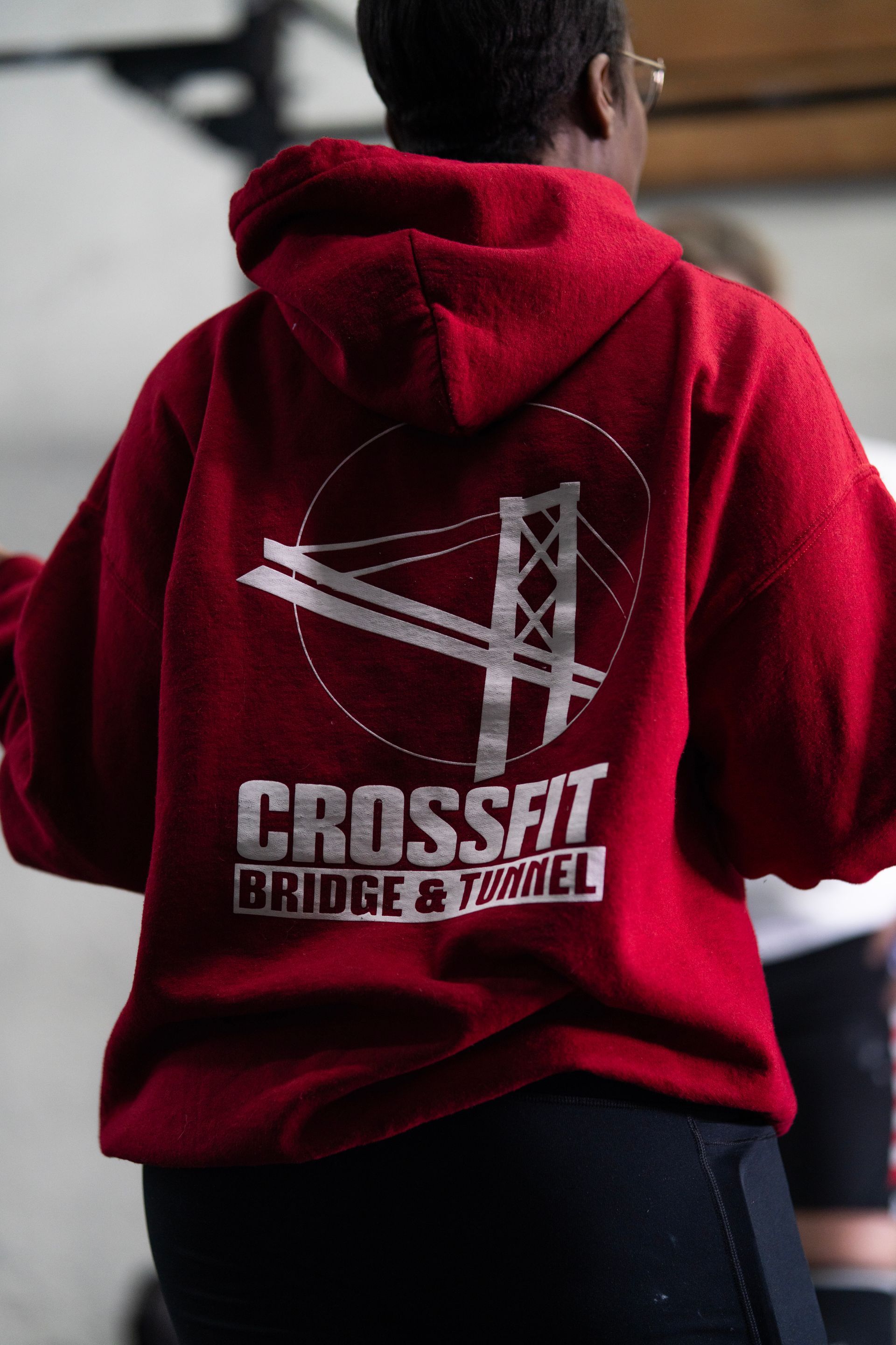 Person in a red CrossFit hoodie seen from behind, standing indoors.