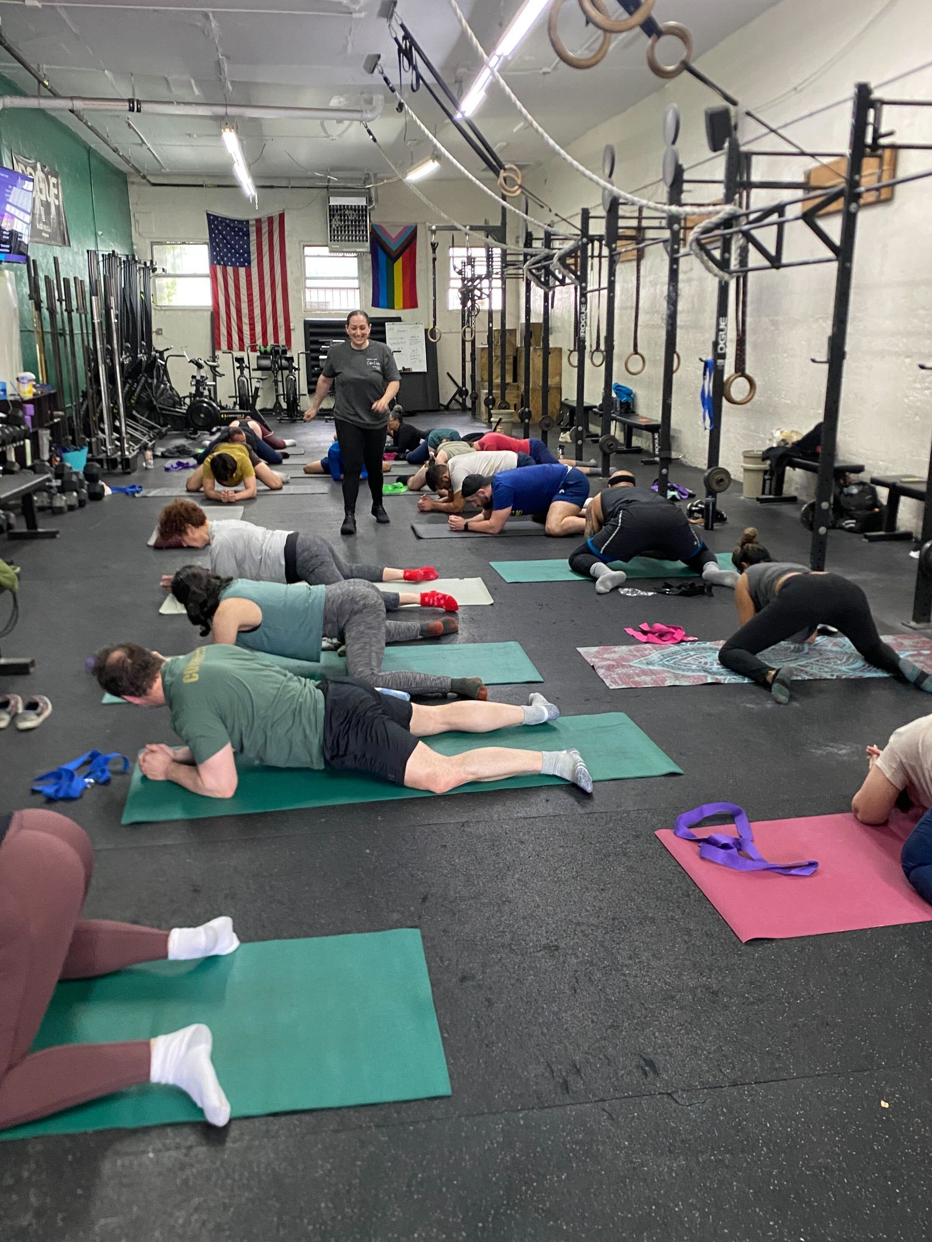 People stretching on mats in a gym while a trainer stands nearby.