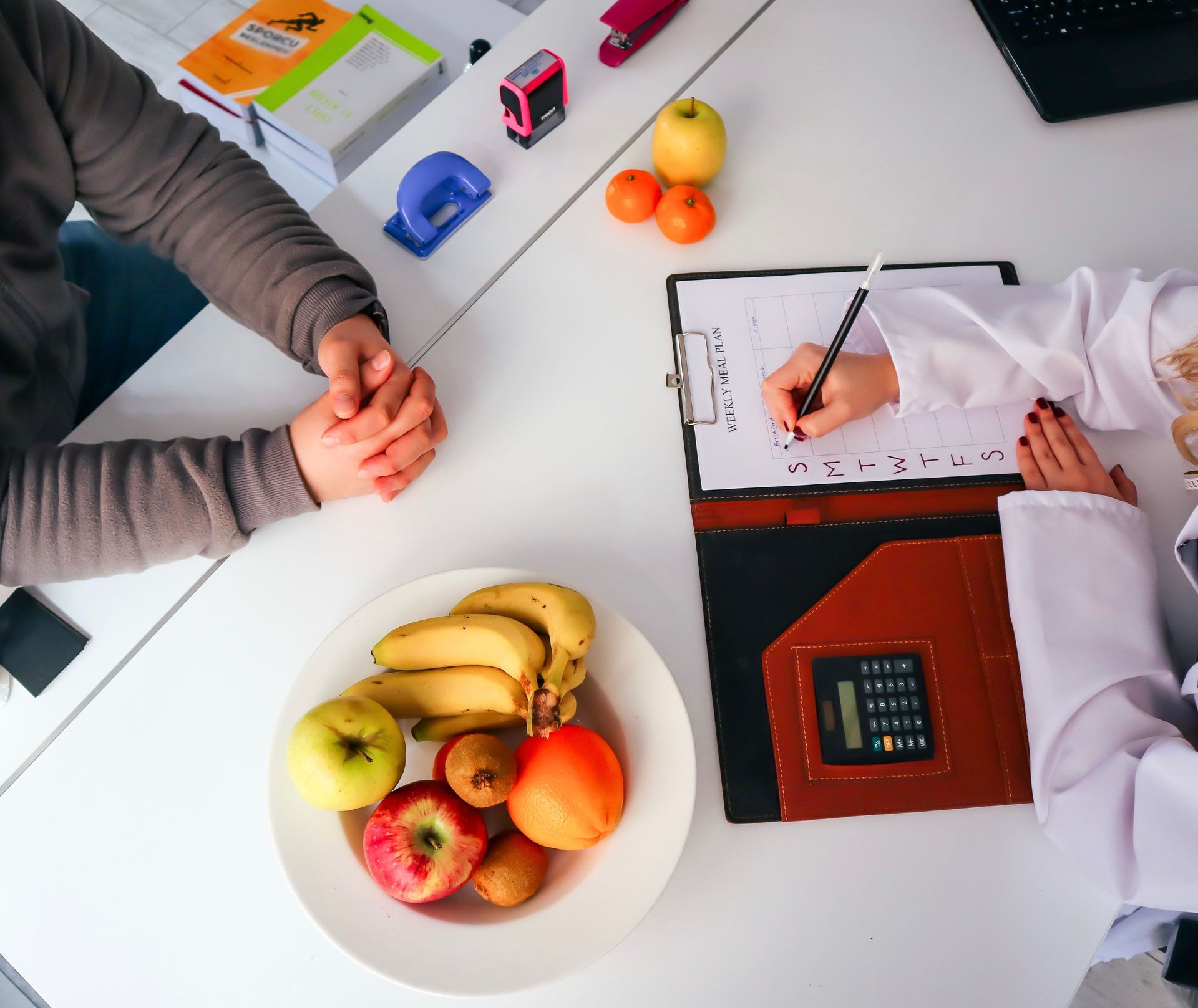 Top-down view of a nutrition assessment with fruit, a hand, and a clipboard on a white table
