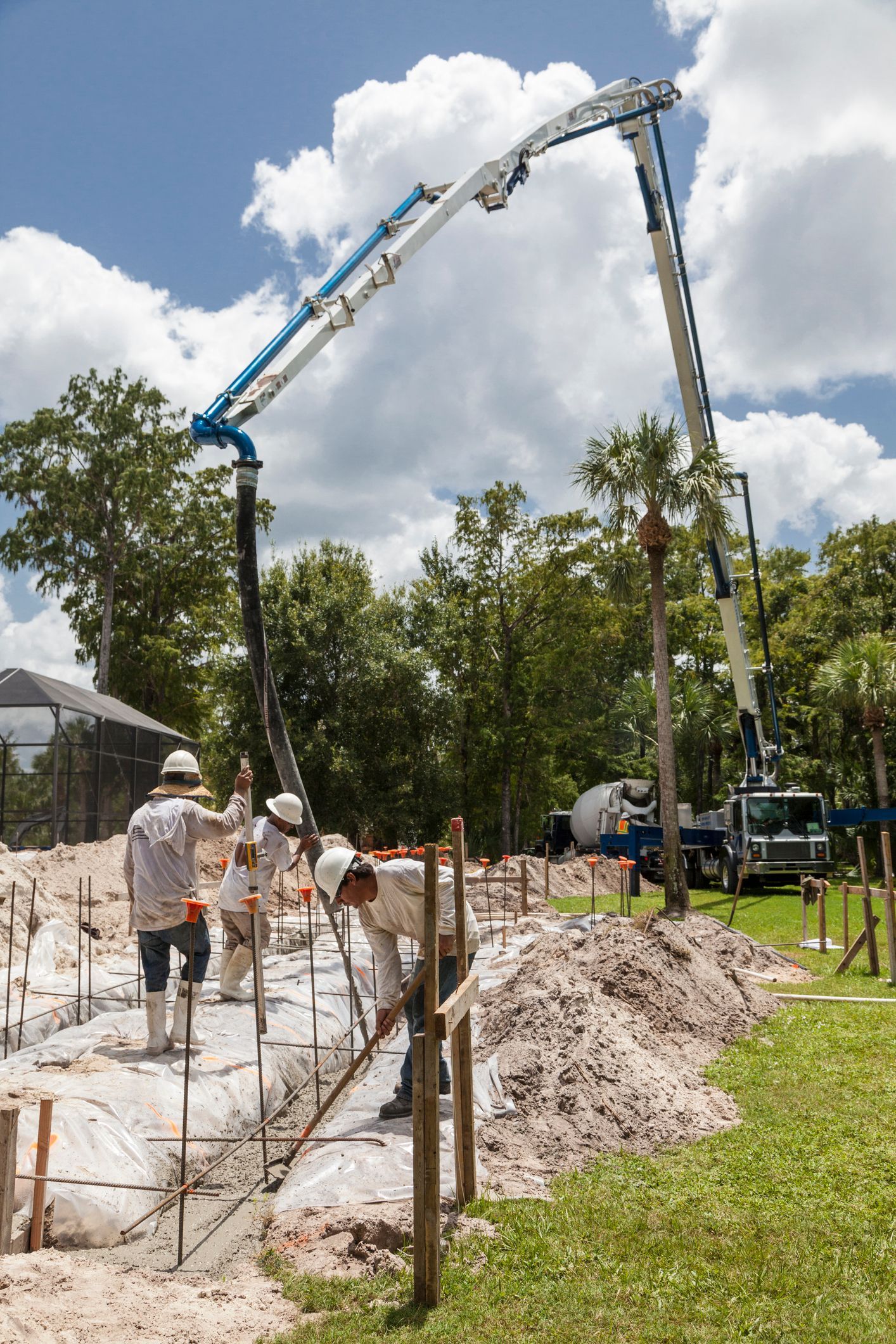 Construction crew performing residential concrete pumping at housing site with large pump hose. Construction crew performing residential concrete pumping at housing site with large pump hose.
