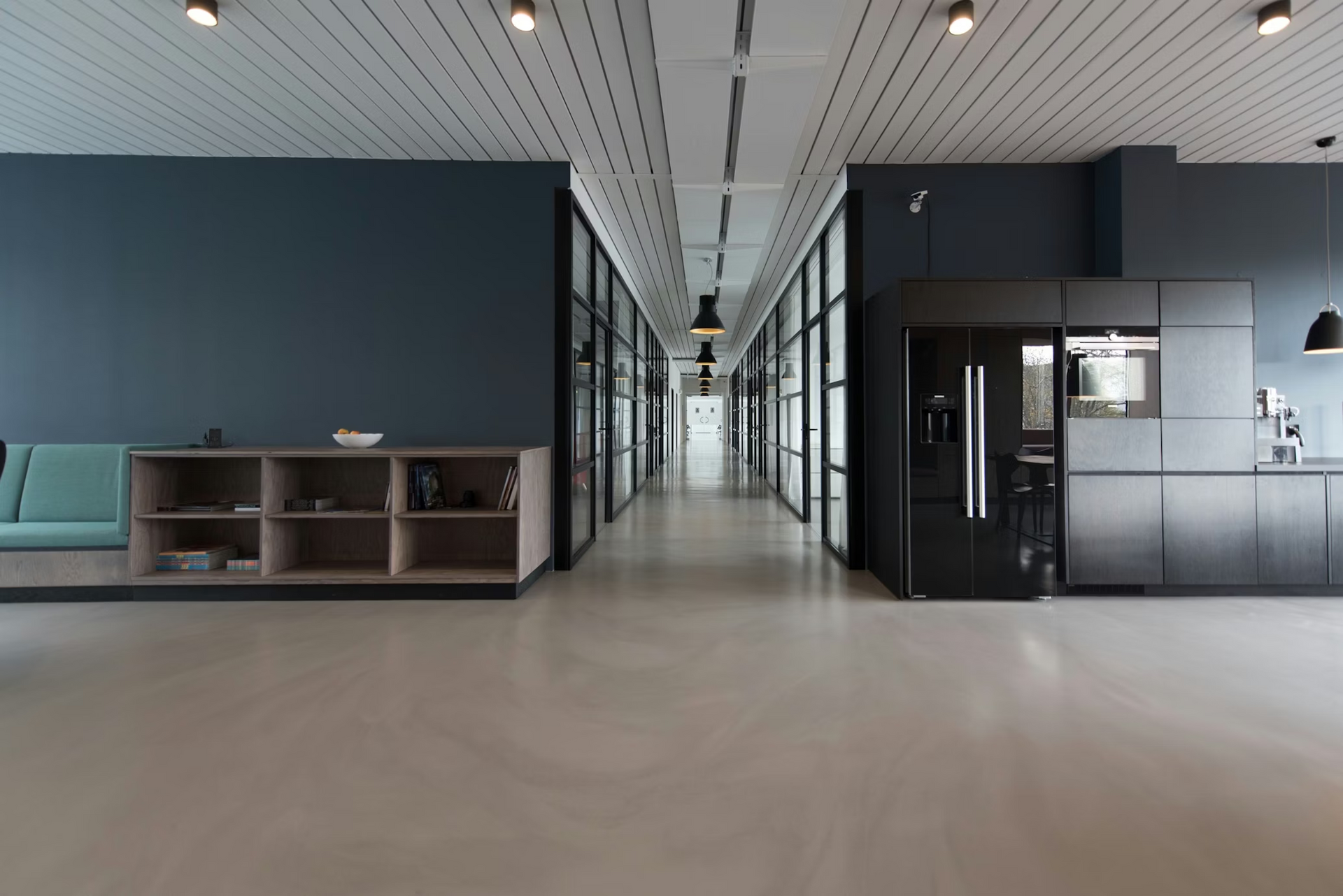 Modern office lobby with dark partitioned rooms, glass walls, and a long central corridor.