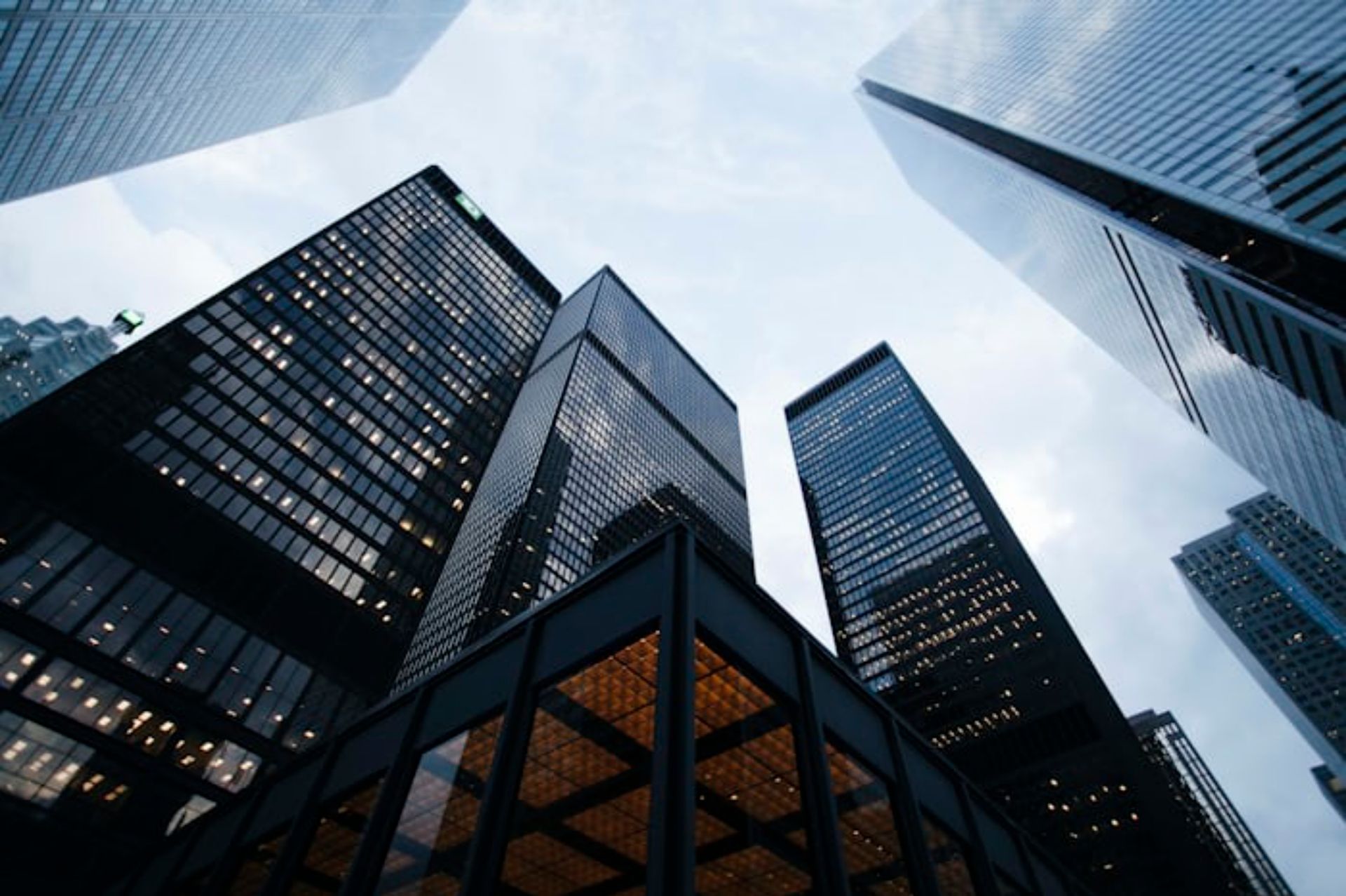 Skyscrapers viewed from below against a cloudy sky, with glass and steel facades.