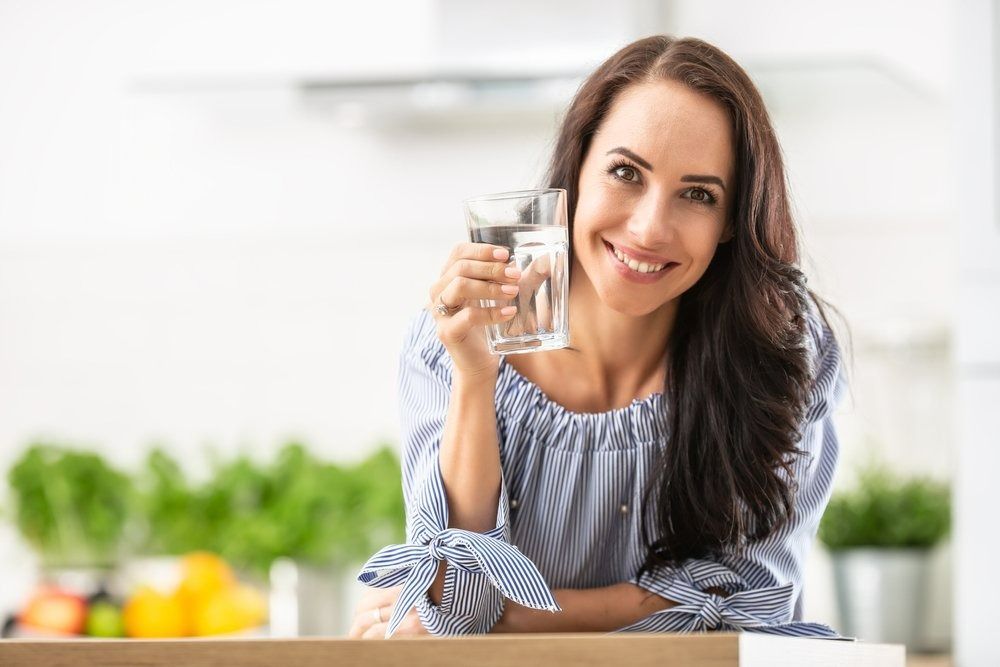 Woman in Kitchen, Smiling, Holding a Glass of Water — The Colonic Coach in Gulliver, QLD