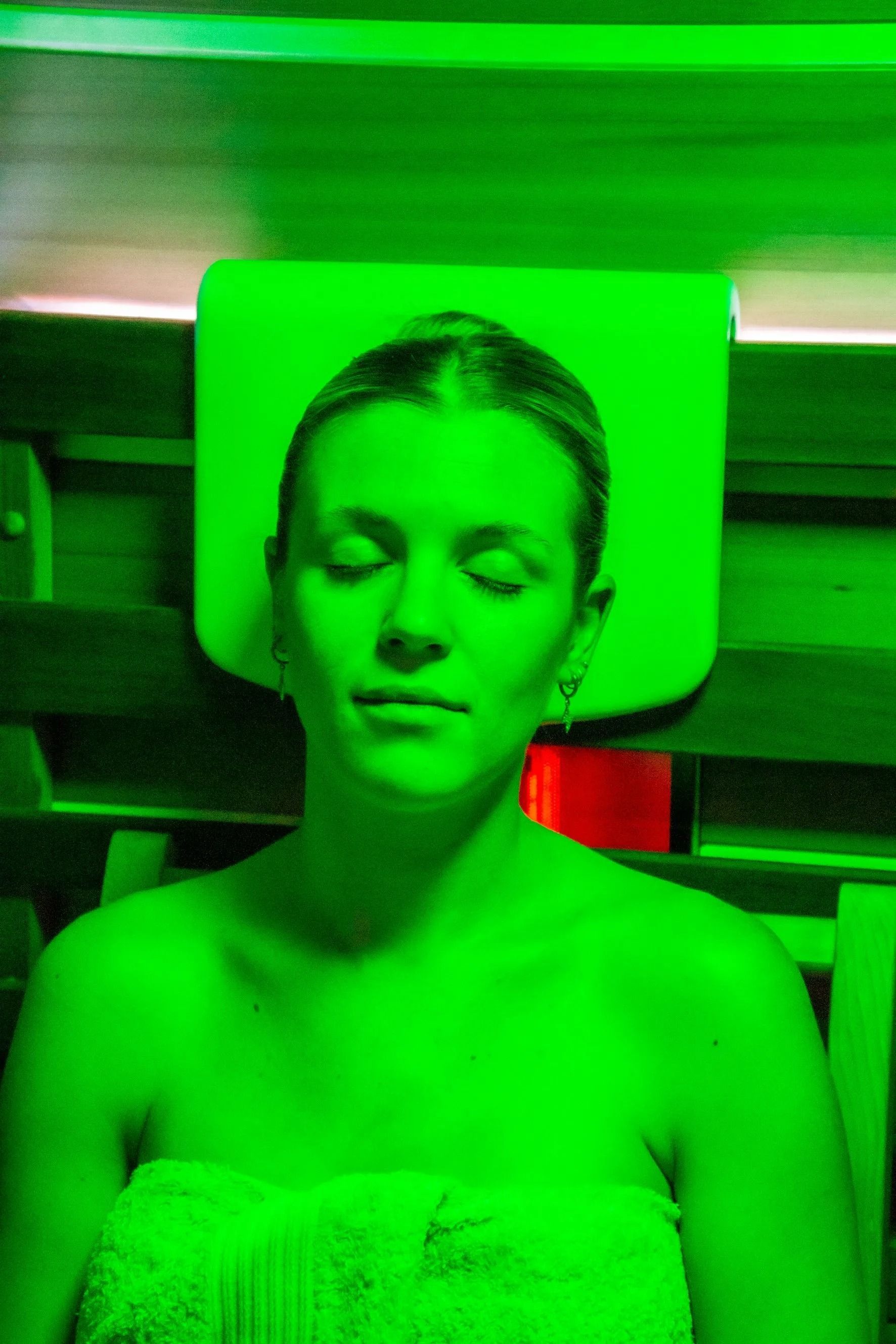 Woman with Eyes Closed Under a Green Light; Wrapped in A Towel — The Colonic Coach in Gulliver, QLD