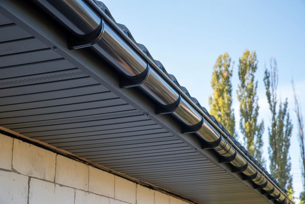Guttered roof eave on a house with blue sky and tall trees in the background