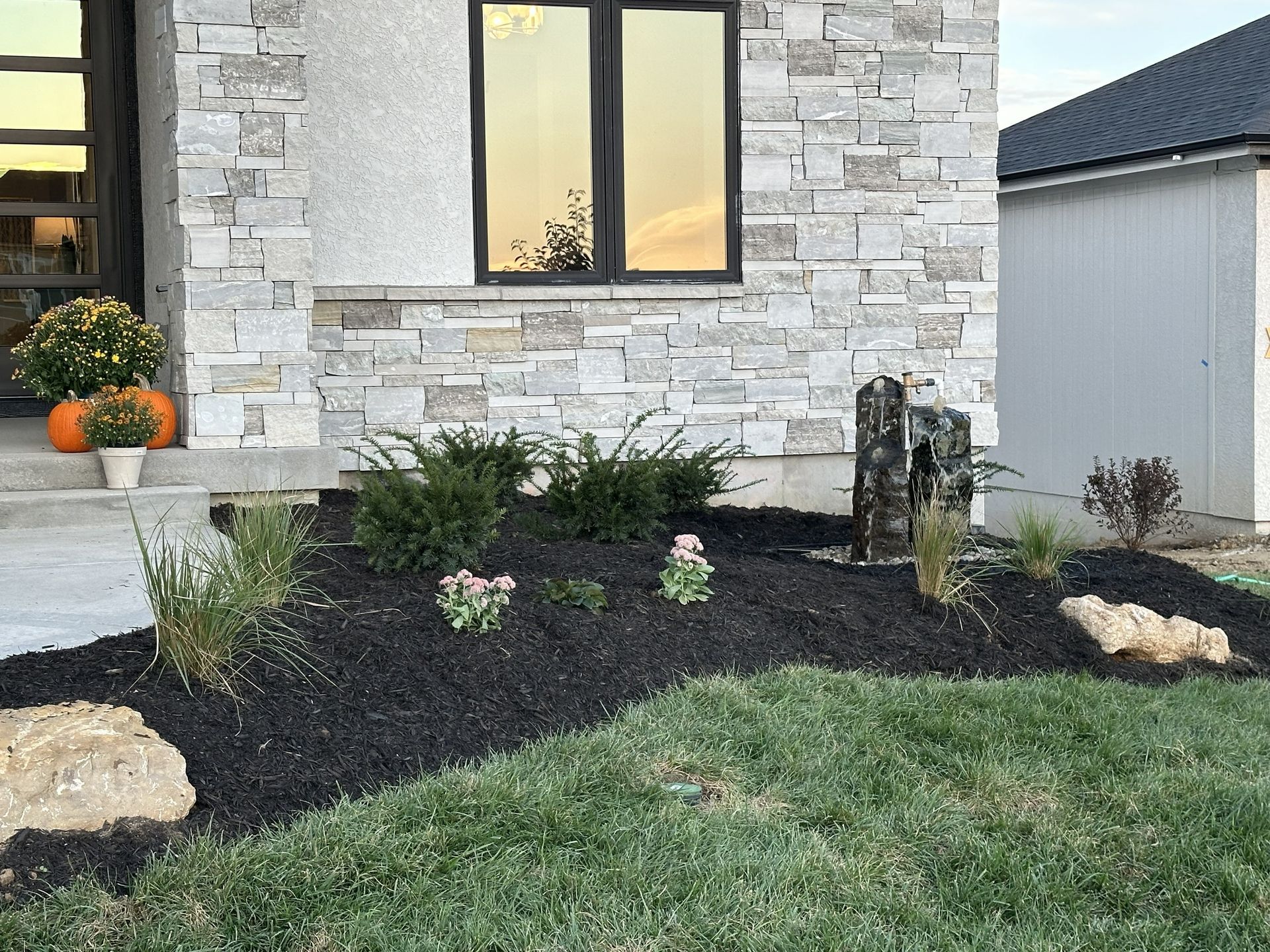 Front yard landscaping with black mulch, shrubs, stone accents, and a house exterior with a window