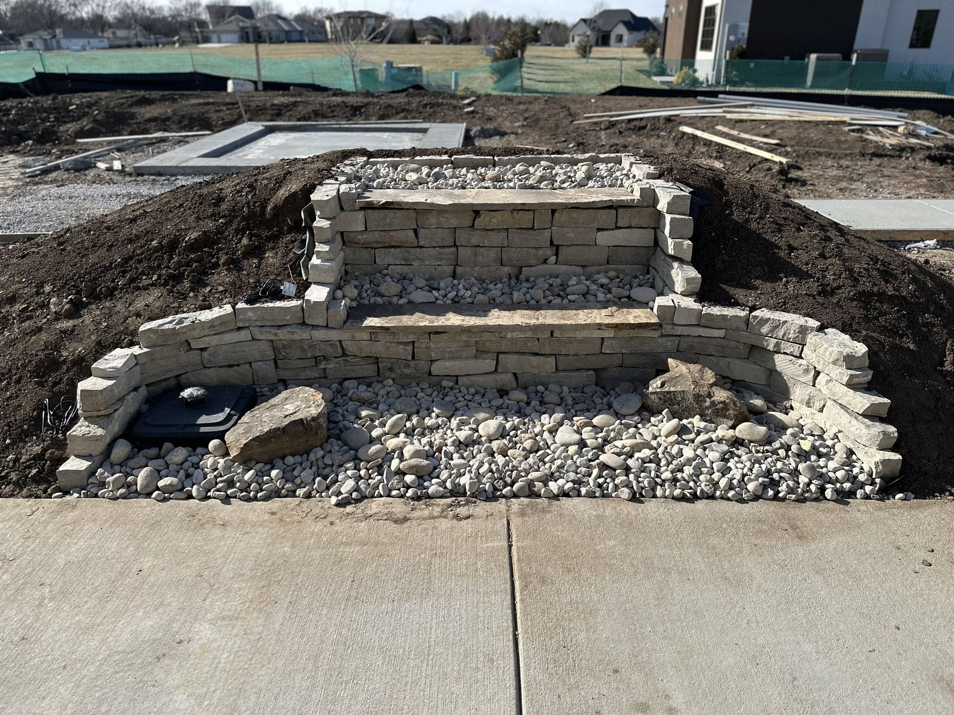 Stone retaining wall and gravel landscaping beside a concrete path in an outdoor construction site