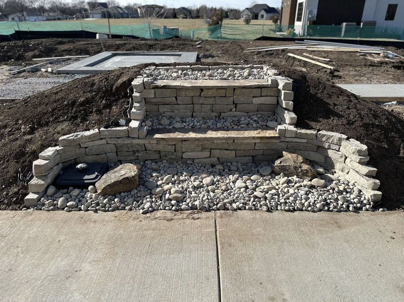 Stone retaining wall and gravel landscaping beside a concrete path in an outdoor construction site