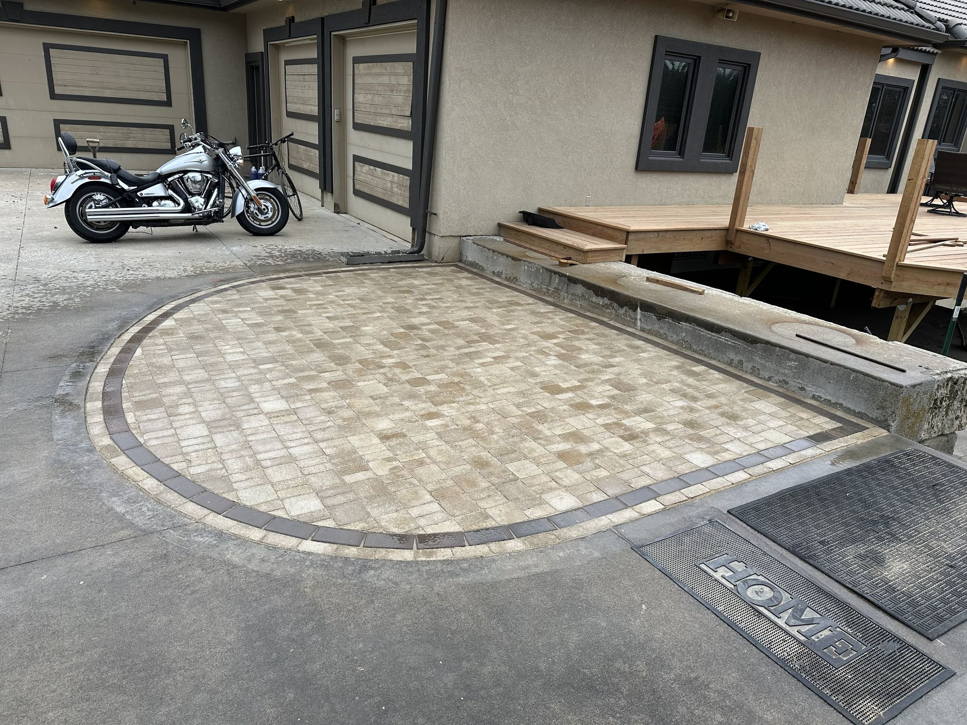 Motorcycle parked beside a tan building with a curved stone driveway and wooden deck.