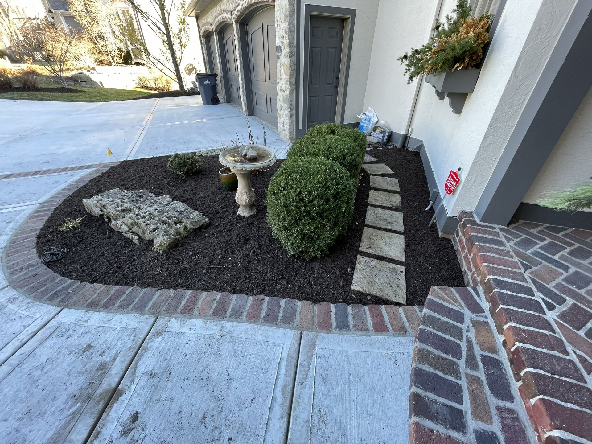 Front walkway with dark mulch, stepping stones, two stone planters, and a small landscaped bed beside a building.
