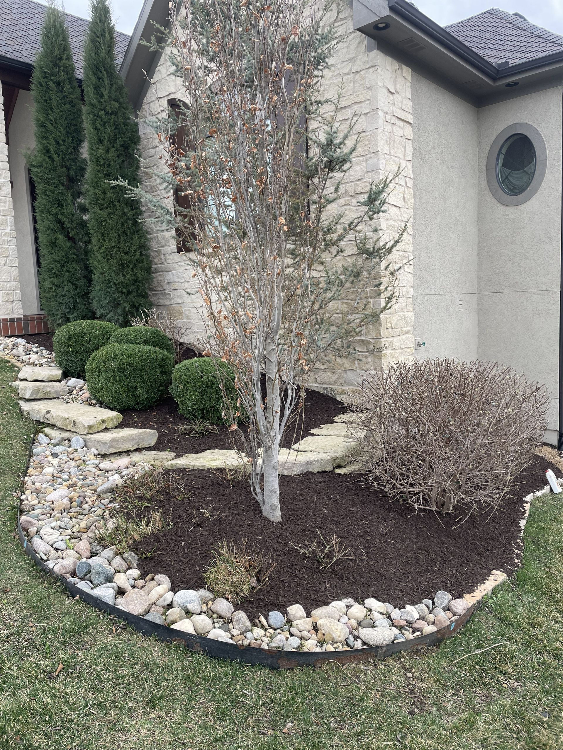 Landscaped front yard with mulch, rocks, shrubs, and a small tree beside a stucco house