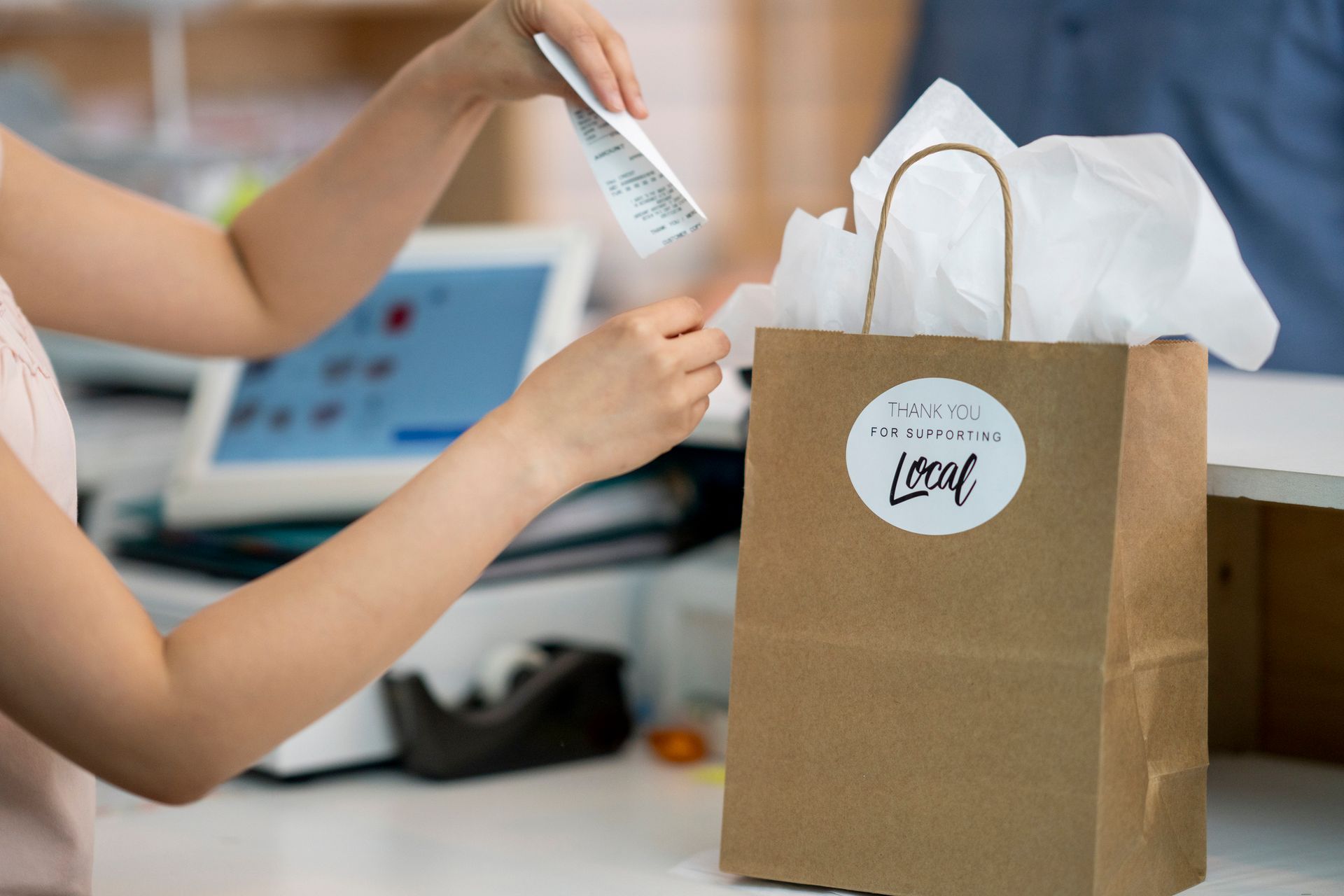 Hands placing a white item into a brown gift bag on a store counter