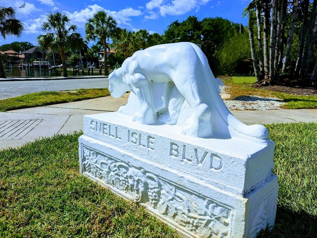 panther statue on a stone base in a sunny park with trees and grass