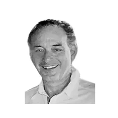 Smiling man in a dark suit jacket and white shirt, standing against a light gray background.